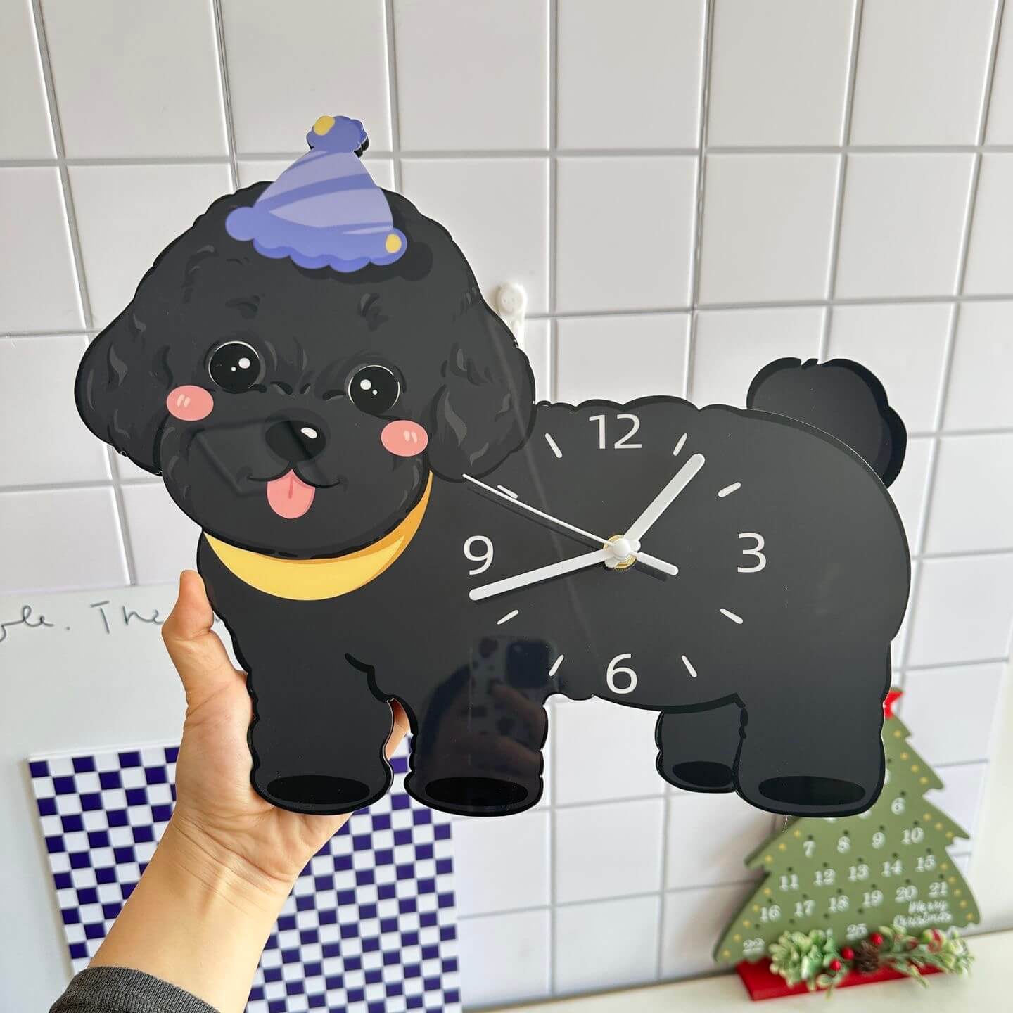 Black poodle wall clock on white tile wall with festive Christmas tree and checkered fabric
