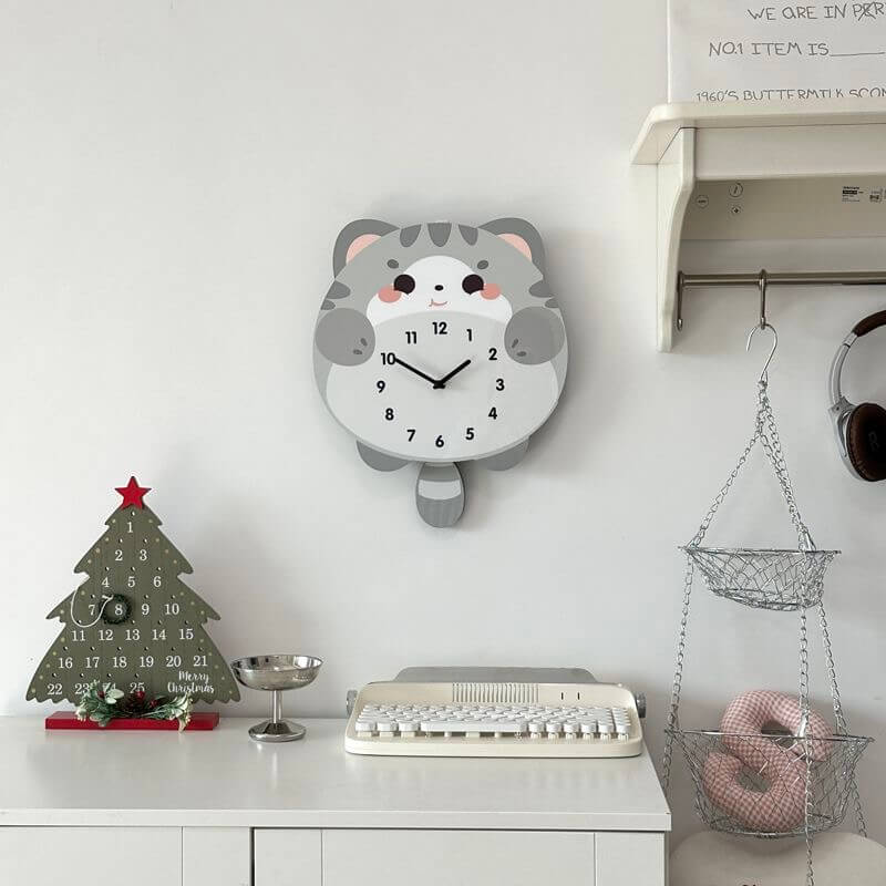 British Shorthair blue cat clock front view on white wall with green plant