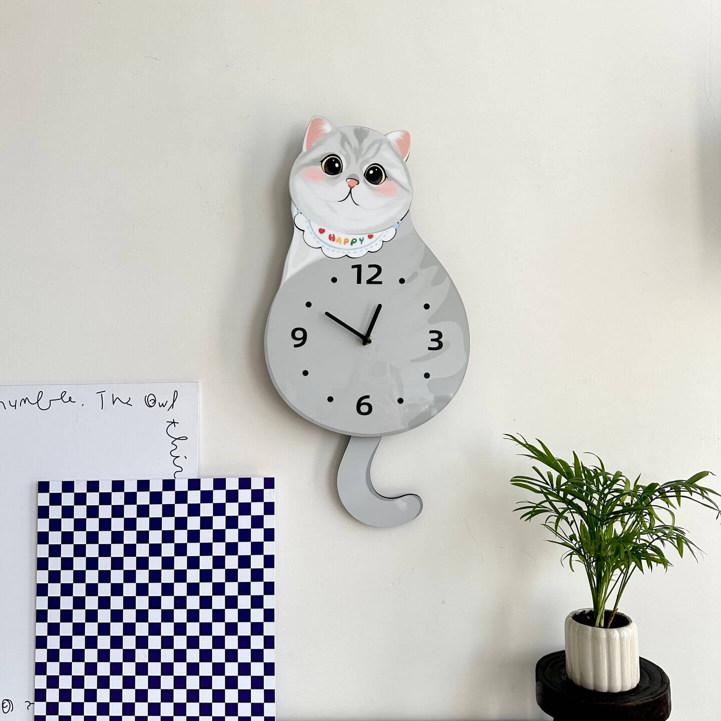 British Shorthair silver shaded clock on white wall with green plant and home decor items