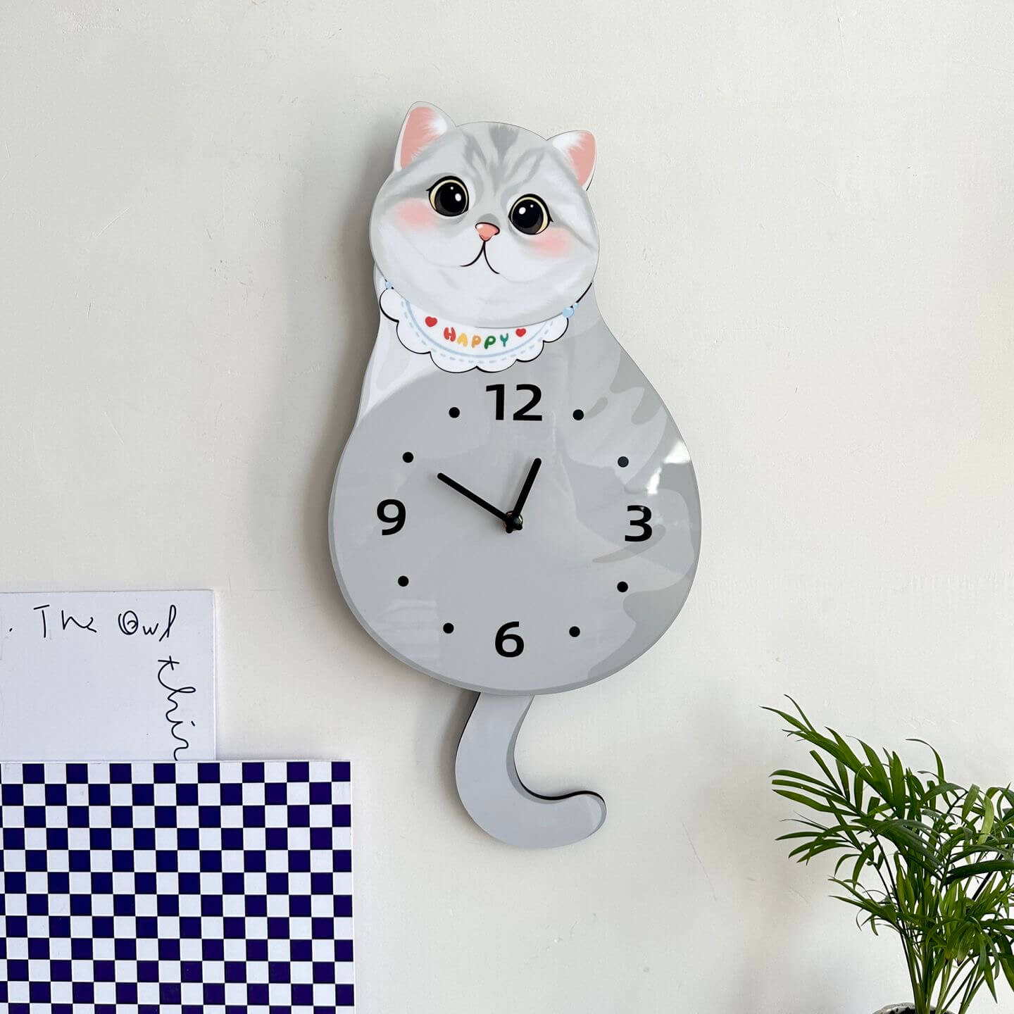 British Shorthair silver shaded wall clock mounted on clean white wall with green plant decor