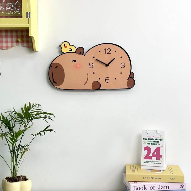 Capybara lying wall clock on cream wall with yellow cabinet, plant, calendar and book stack