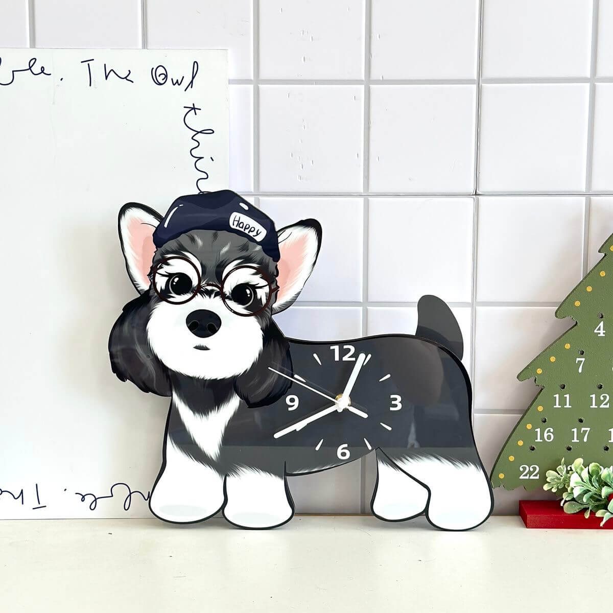 Schnauzer dog clock on white tiled wall beside a Christmas tree advent calendar