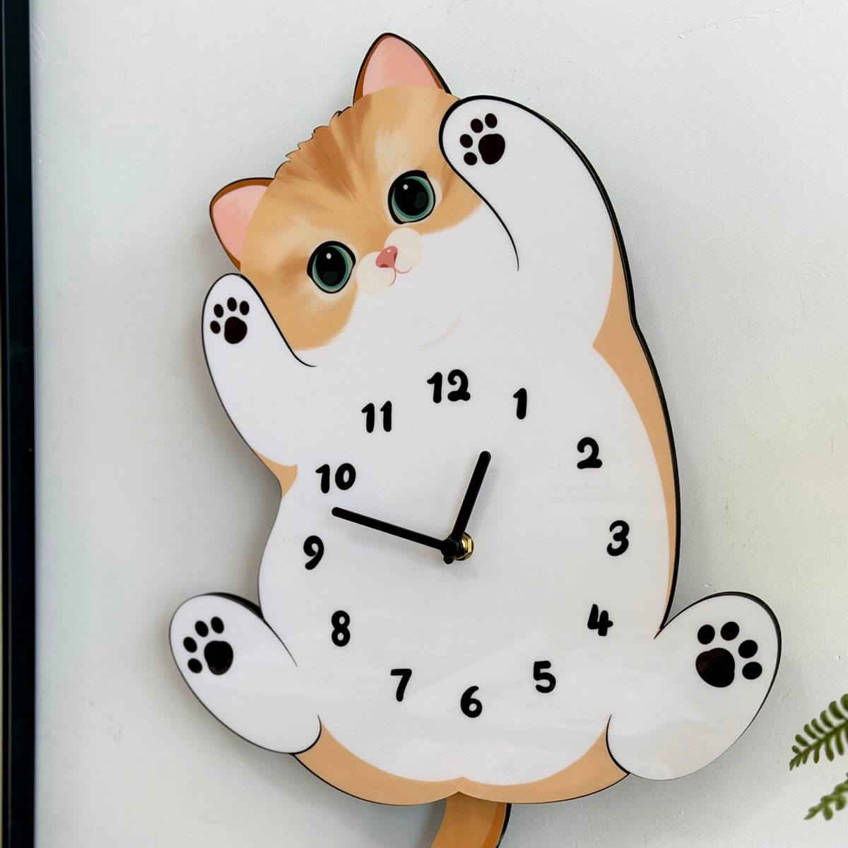 Orange tabby cat clock on white wall with green plant and decorative items
