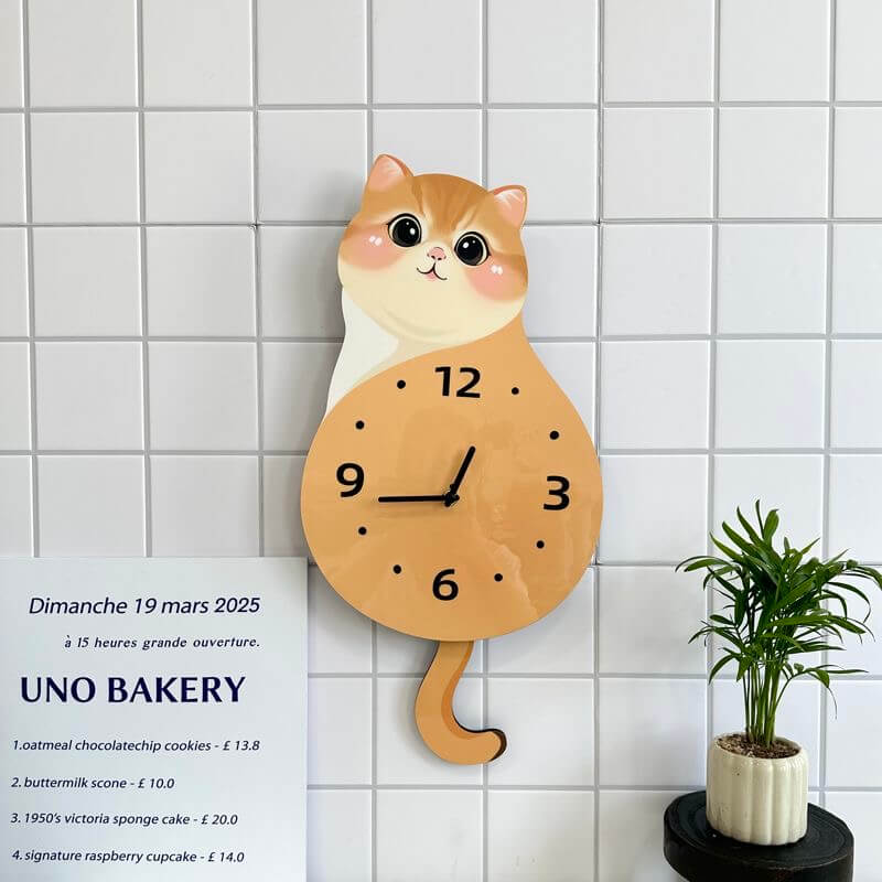 Orange tabby sitting cat wall clock mounted on clean white wall with green plant decor