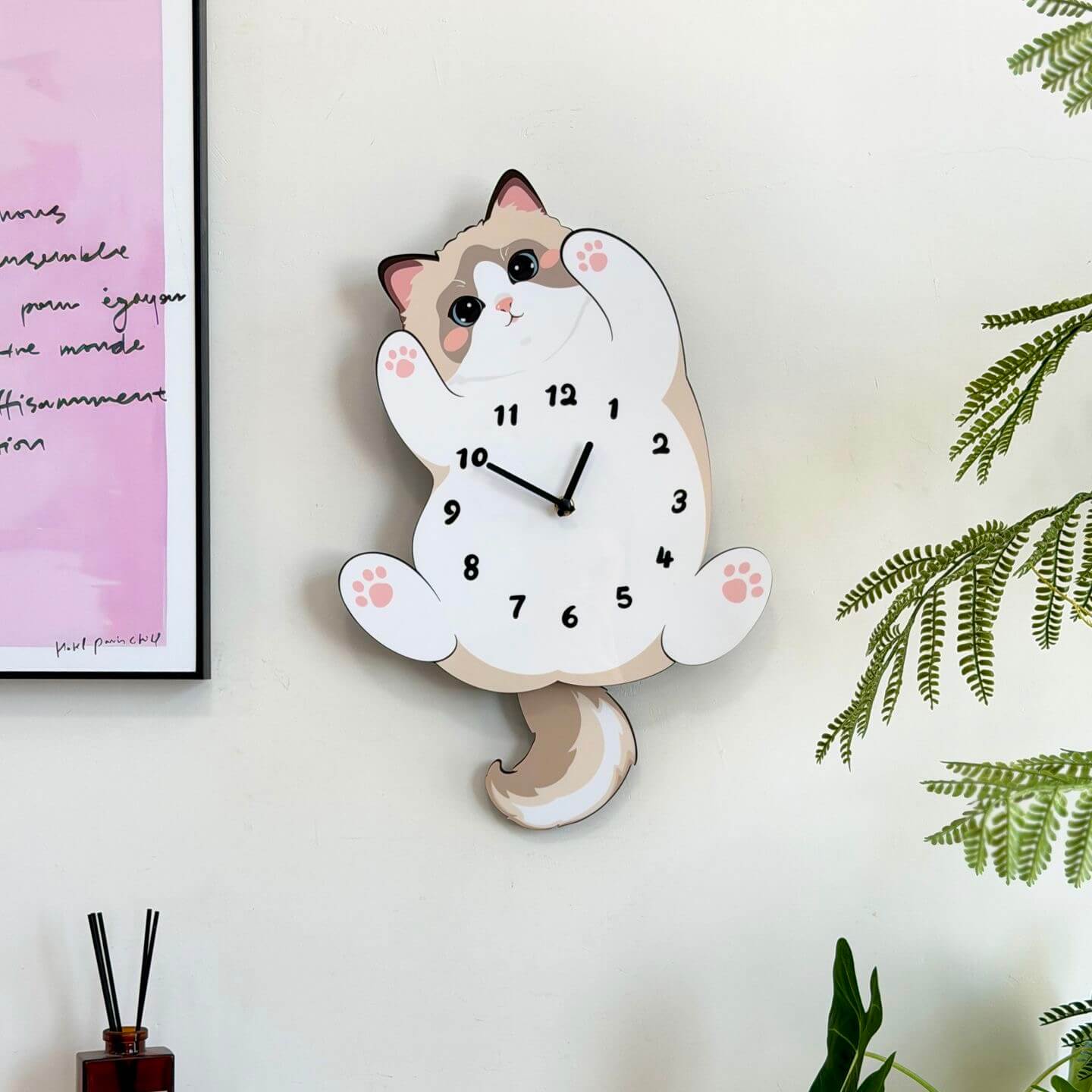 Ragdoll cat pet clock on cream wall with pink abstract art print and green fern decor