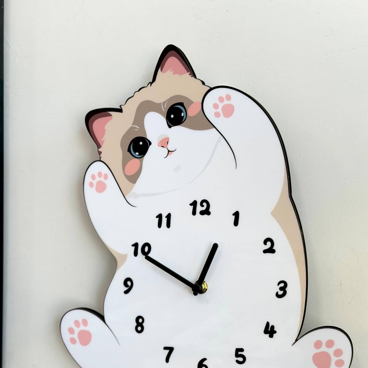 Ragdoll cat clock on cream wall with decorative items and houseplant