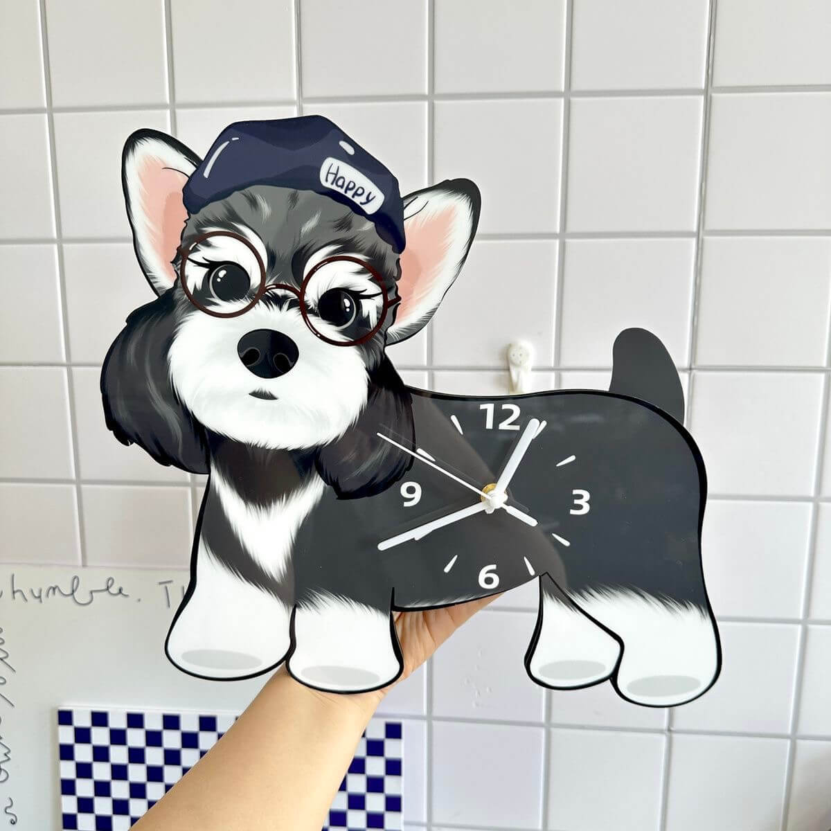Hand holding the Schnauzer dog-shaped wall clock in front of a white tiled wall